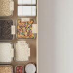 Neatly organized pantry shelf with clear containers of staples and simple week labels in soft morning light.